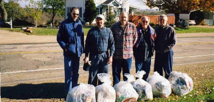 five volunteers stand in front of six bags of collected trash in front of two-lane Highway ID.