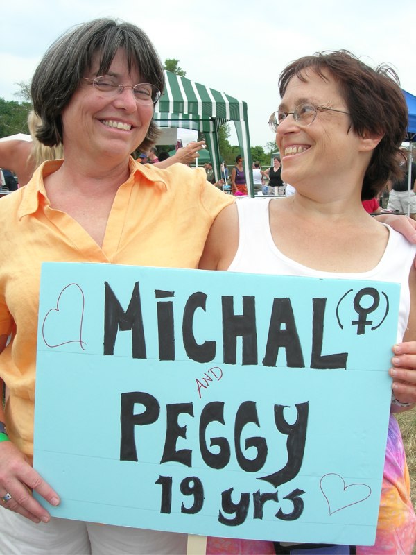 Michal and Peggy stand smiling and holding their sign indicating they've been together 19 years.